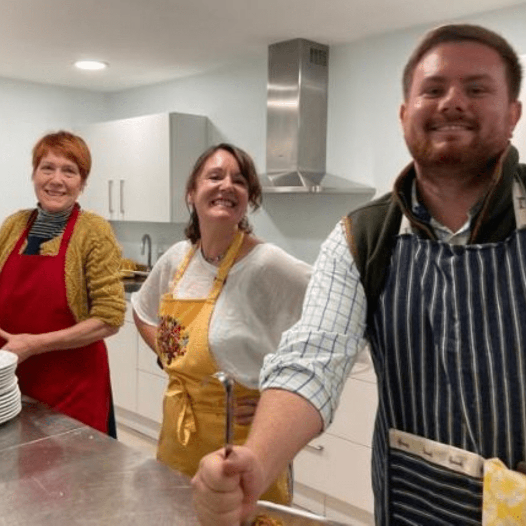 Three volunteers in aprons preparing food for the lunch club